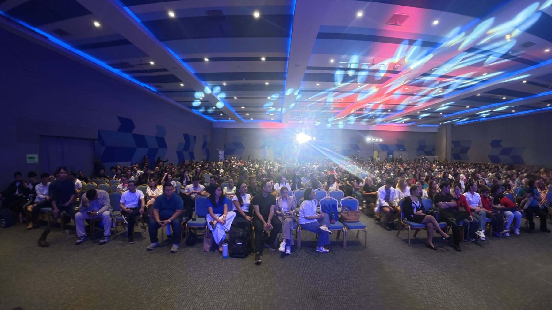 The whole hall facing the stage, a beam of light cutting across the room