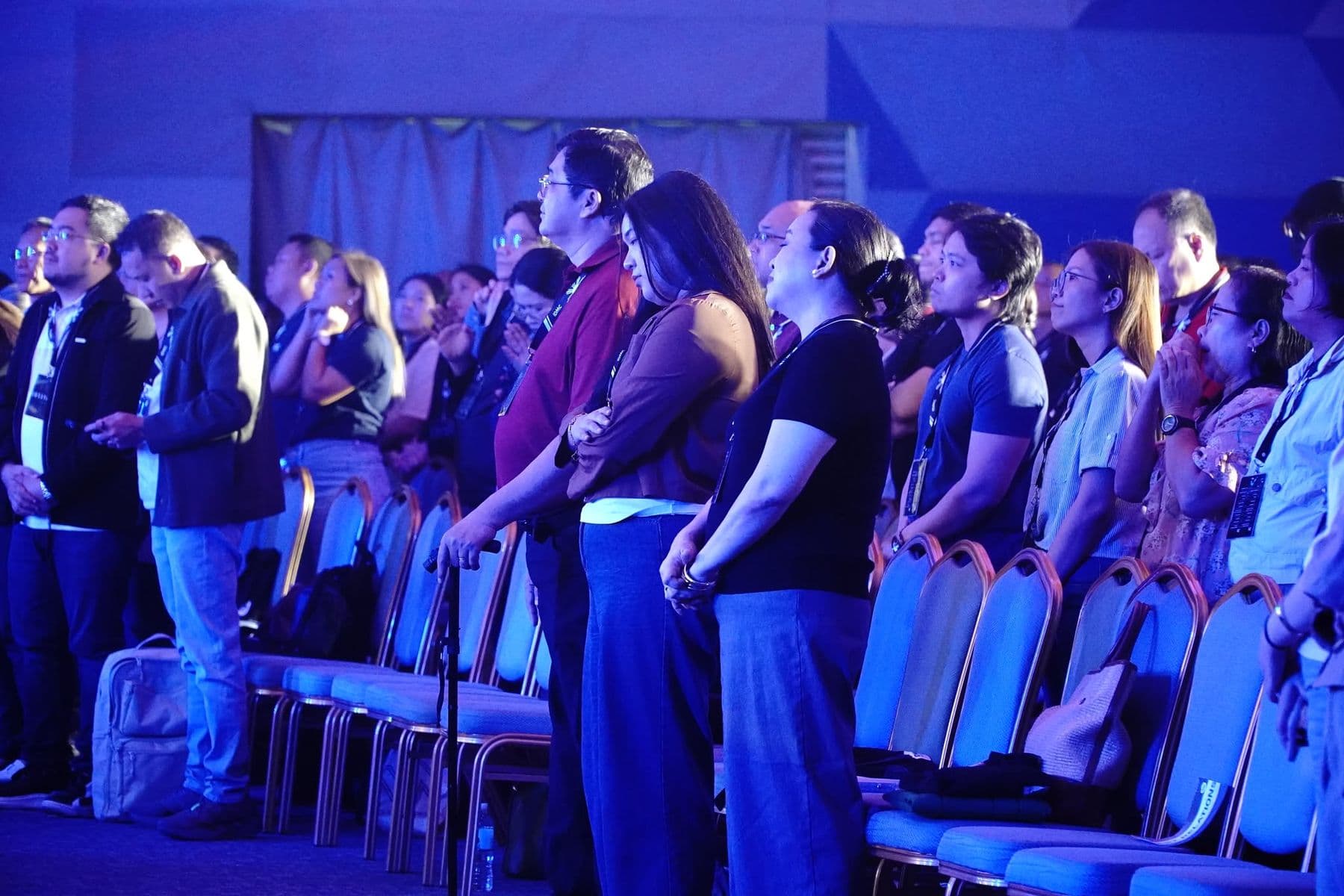 A row of delegates standing with heads bowed in prayer