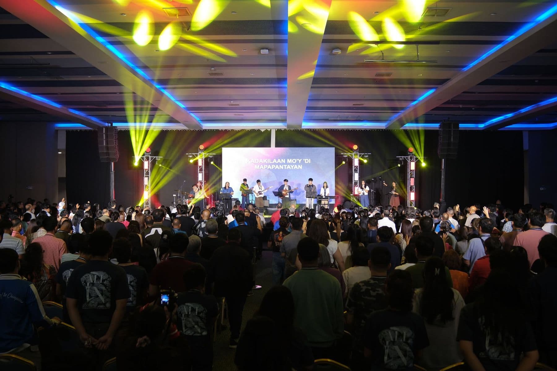The hall during evening worship, yellow stage lights fanning over the crowd